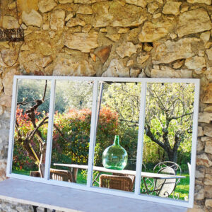 Miroir verrière grand format en métal blanc mat comme une fenêtre ouverte sur l'extérieur. Forme inspirée de l'esprit scandinave et du style atelier, peut être fixé dedans ou dehors